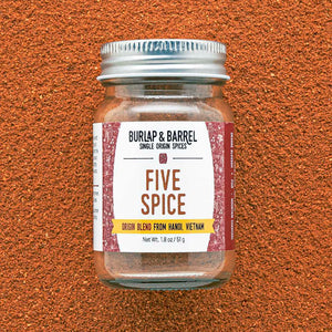 A glass jar with a metal lid labeled 'FIVE SPICE' from Burlap & Barrel on an orange textured background.