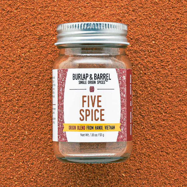 A glass jar with a metal lid labeled 'FIVE SPICE' from Burlap & Barrel on an orange textured background.