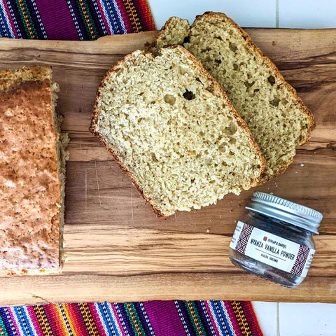 Sliced zucchini bread and whole wheat bread on wooden board with jar of seasoning and colorful woven textiles.