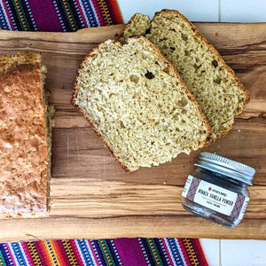 Sliced zucchini bread and whole wheat bread on wooden board with jar of seasoning and colorful woven textiles.